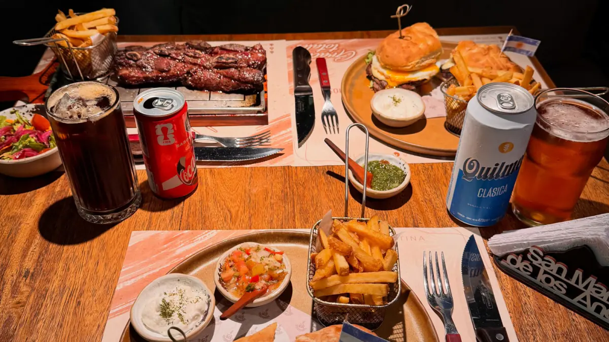 Mesa servida en Del Sur: asado de tira, sánguche de lomito, papas fritas y cerveza Quilmes